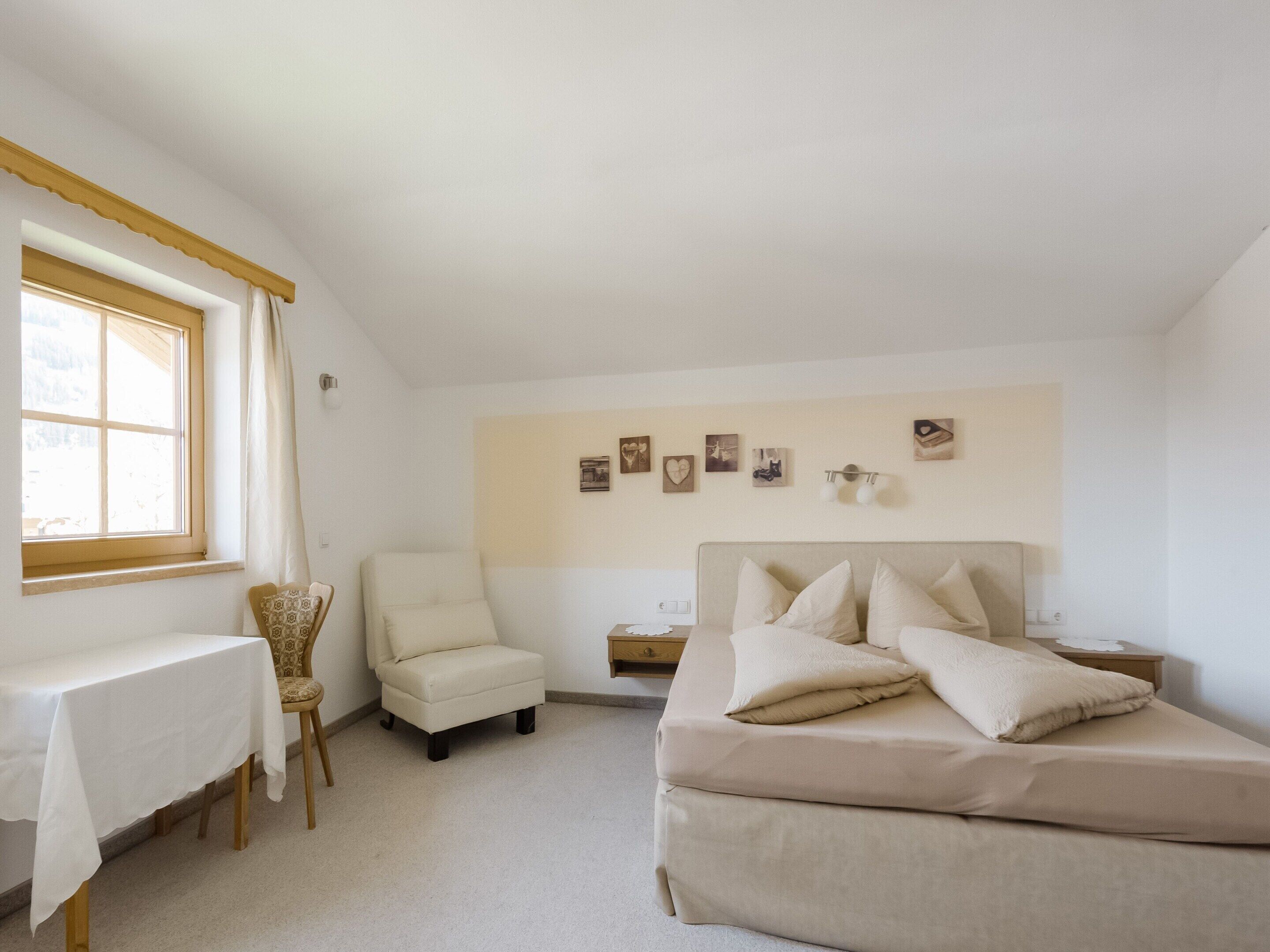 Een slaapkamer met een bed, een stoel, een tafel en een raam.