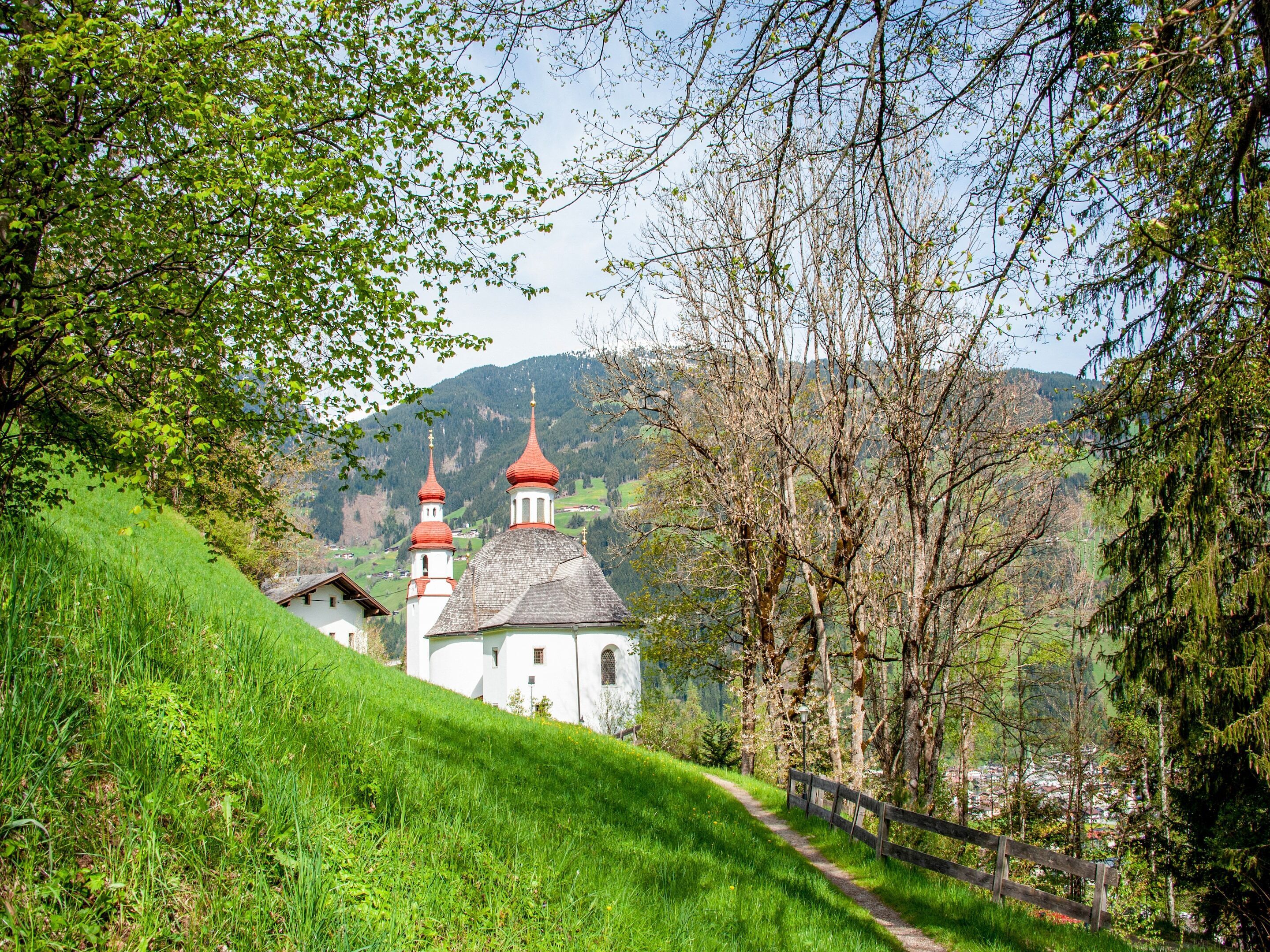Una iglesia con dos cúpulas rojas, rodeada de abundante vegetación y un sendero que lleva a ella.