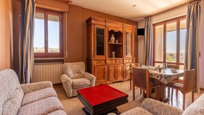A living room with a sofa set, a red ottoman, a wooden cabinet, and a dining table with chairs. - Nice Apartment in Tuoro sul Trasimeno With Pool (Tuoro sul Trasimeno)