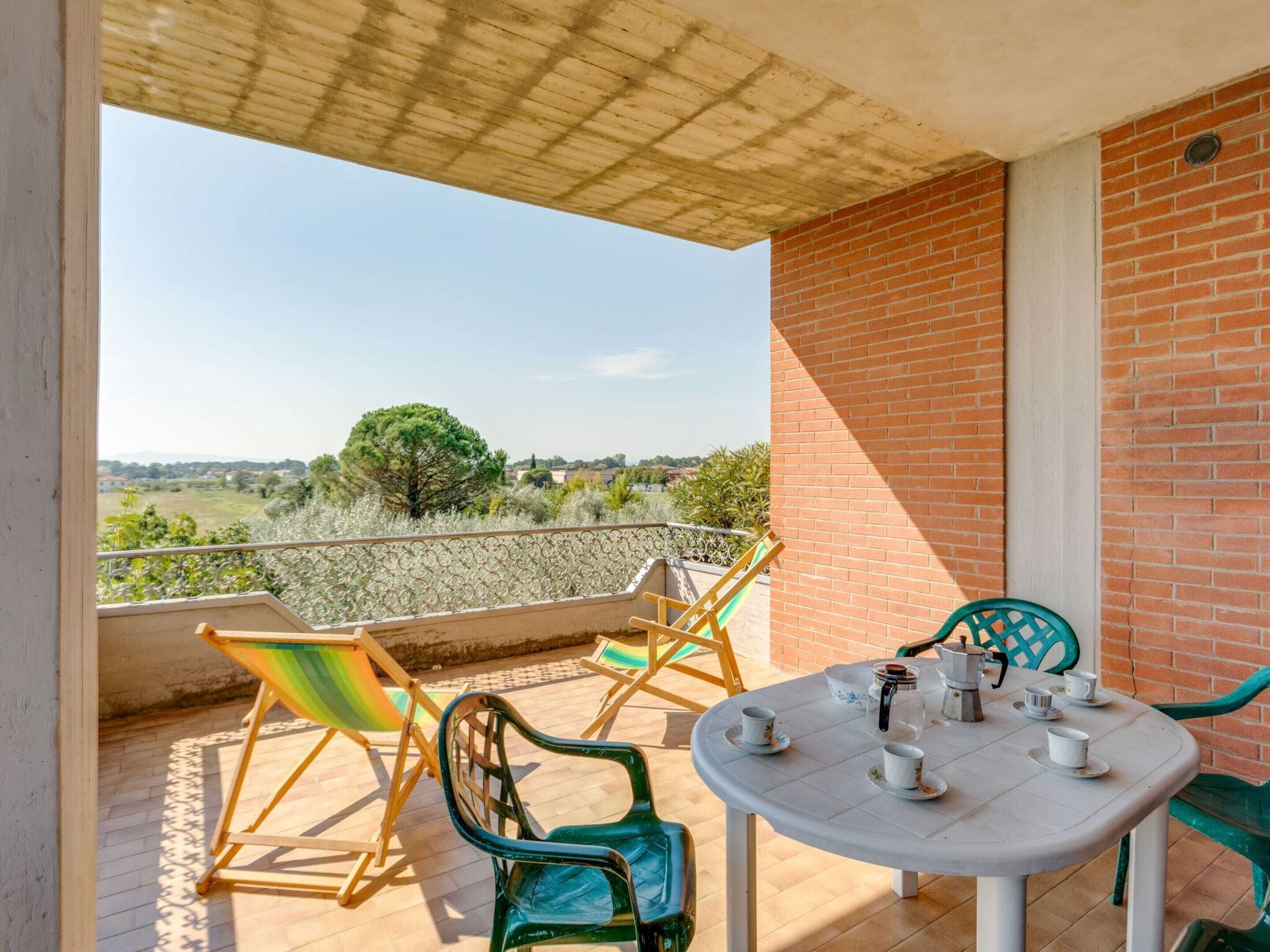 A balcony with a table set for tea, chairs, and a view of the countryside.