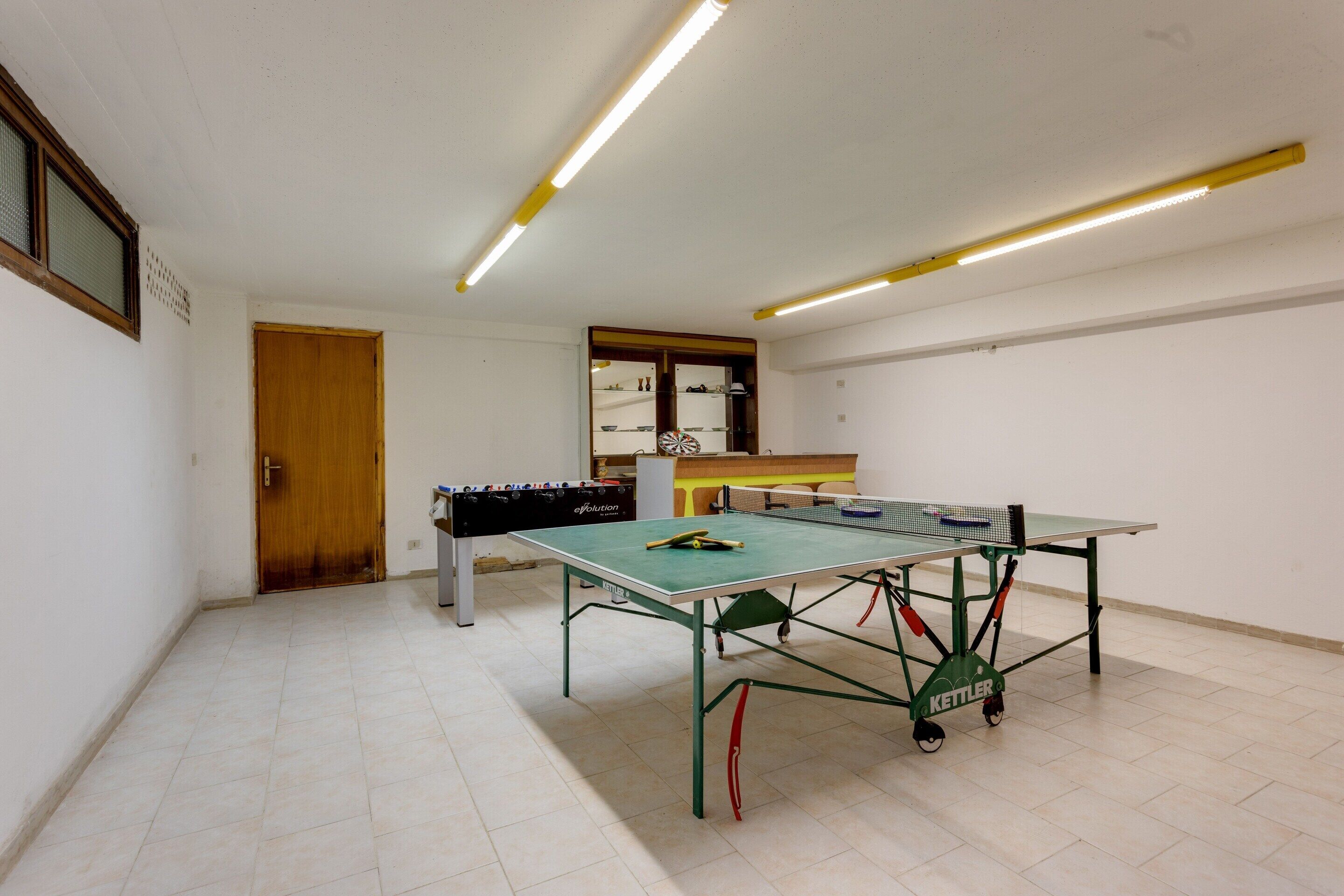 Et værelse med et pingpongbord, et bordfodboldbord og et tekøkken.
