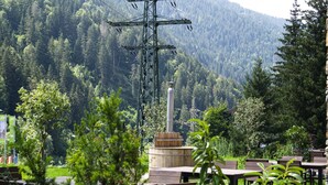 An outdoor seating area with tables and chairs, surrounded by greenery and a mountainous backdrop. - Chalet Montafon in Gaschurn With Sauna (Gaschurn)