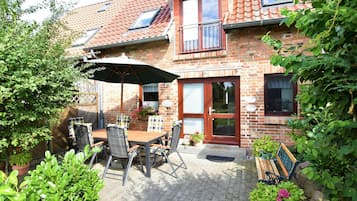 A brick house with a tiled roof, a balcony, and a patio with a table and chairs.