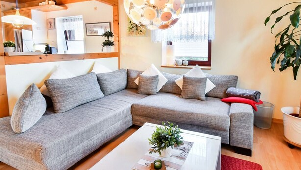 Ein modernes Wohnzimmer mit einem grauen Ecksofa, einem weißen Couchtisch und einem roten Teppich.