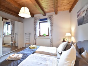 Ein Schlafzimmer mit zwei Betten, einem Fenster mit Vorhängen, einem Heizkörper, einer Hartsreppe, einem Nachttisch mit Lampe und einem Spiegel.