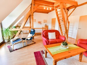 A spacious loft with a high ceiling, wooden beams, a red leather sofa, a blue chair, and a wooden table. - Fabelhaftes Ferienhaus in Thorstorf in Meeresnaehe (Warnow)