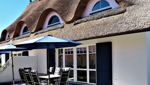 A thatched-roof house with a patio area featuring a table and chairs, and a large umbrella. - Cozy Holiday Home in Rerik With Terrace (Rerik)