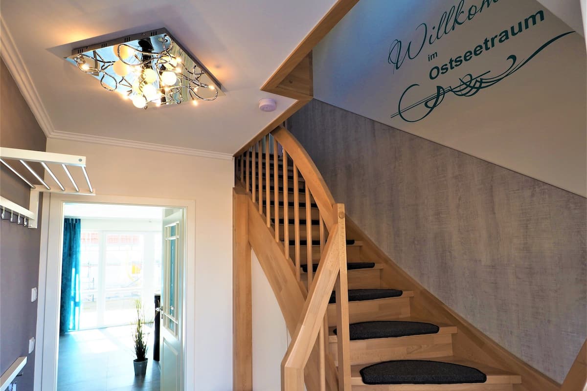 A wooden staircase with black cushioned steps leading to a landing with a decorative light fixture.