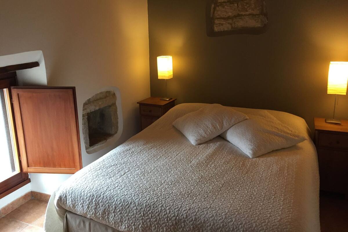 A neatly made bed with a textured blanket and pillows, two bedside lamps, a stone wall decoration, and a wooden door.