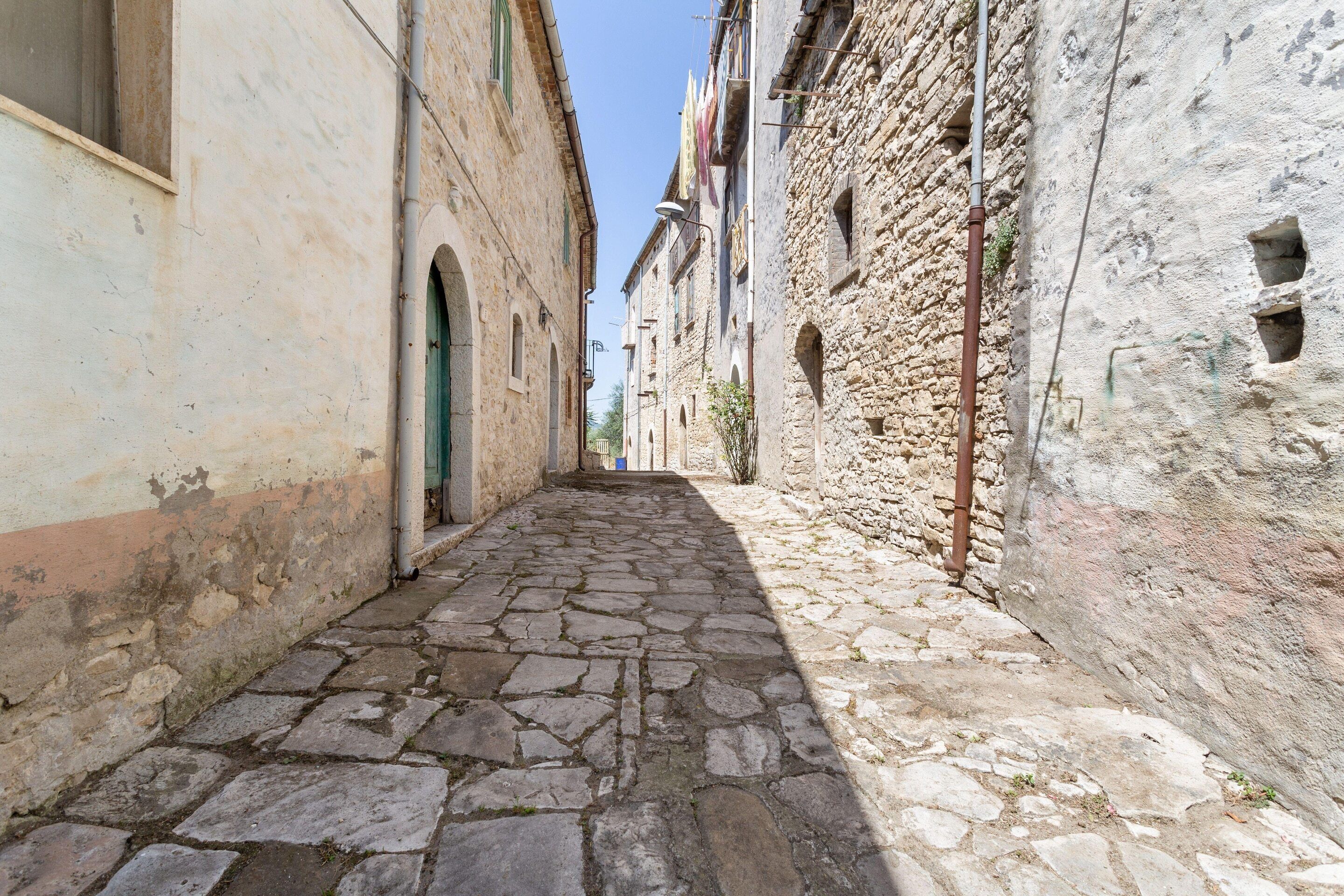 A narrow cobblestone street flanked by historic stone buildings with arched doorways and windows.