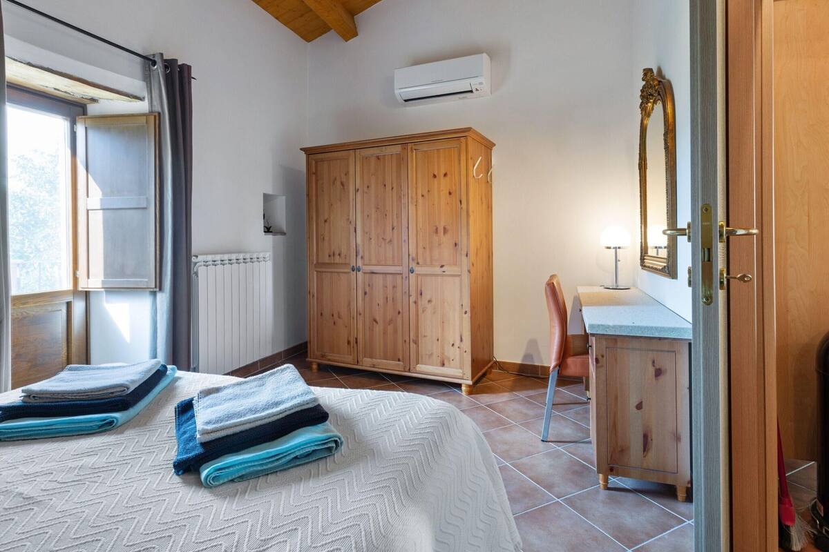 A bedroom with a bed, a wooden wardrobe, a radiator, and a window with curtains.