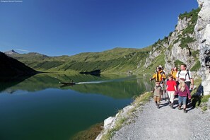 Un grupo de personas en un sendero para excursionistas junto a un lago, con montañas al fondo.