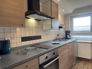 Eine moderne Küche mit Gasherd, integriertem Backofen, Spüle und einem Fenster mit Jalousien.