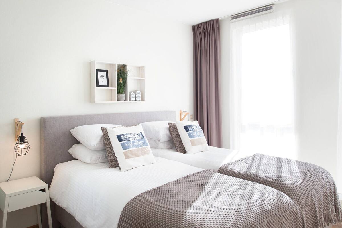 A hotel room with a bed, bedside table, and a wall-mounted shelf with decorative items.