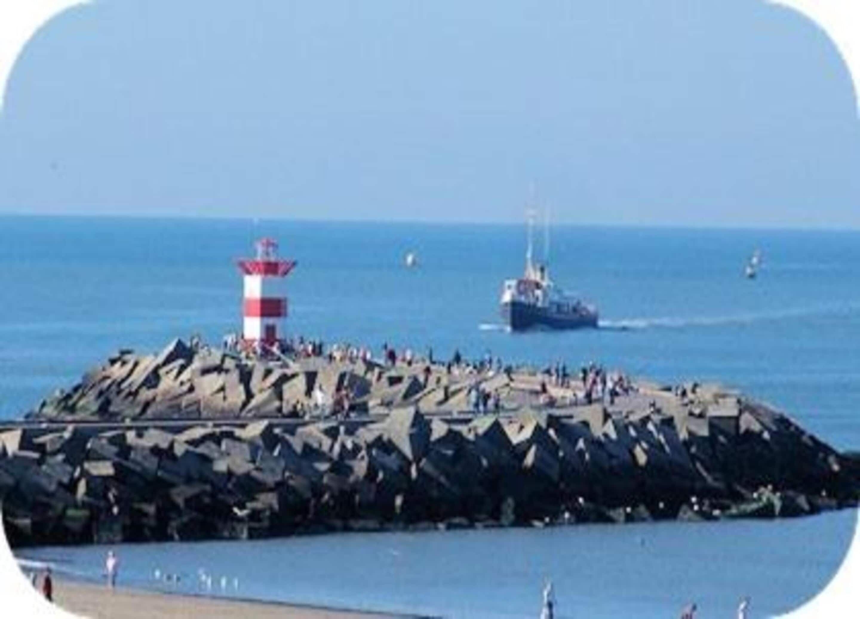 A rocky breakwater with a lighthouse, a boat, and people on the shore.