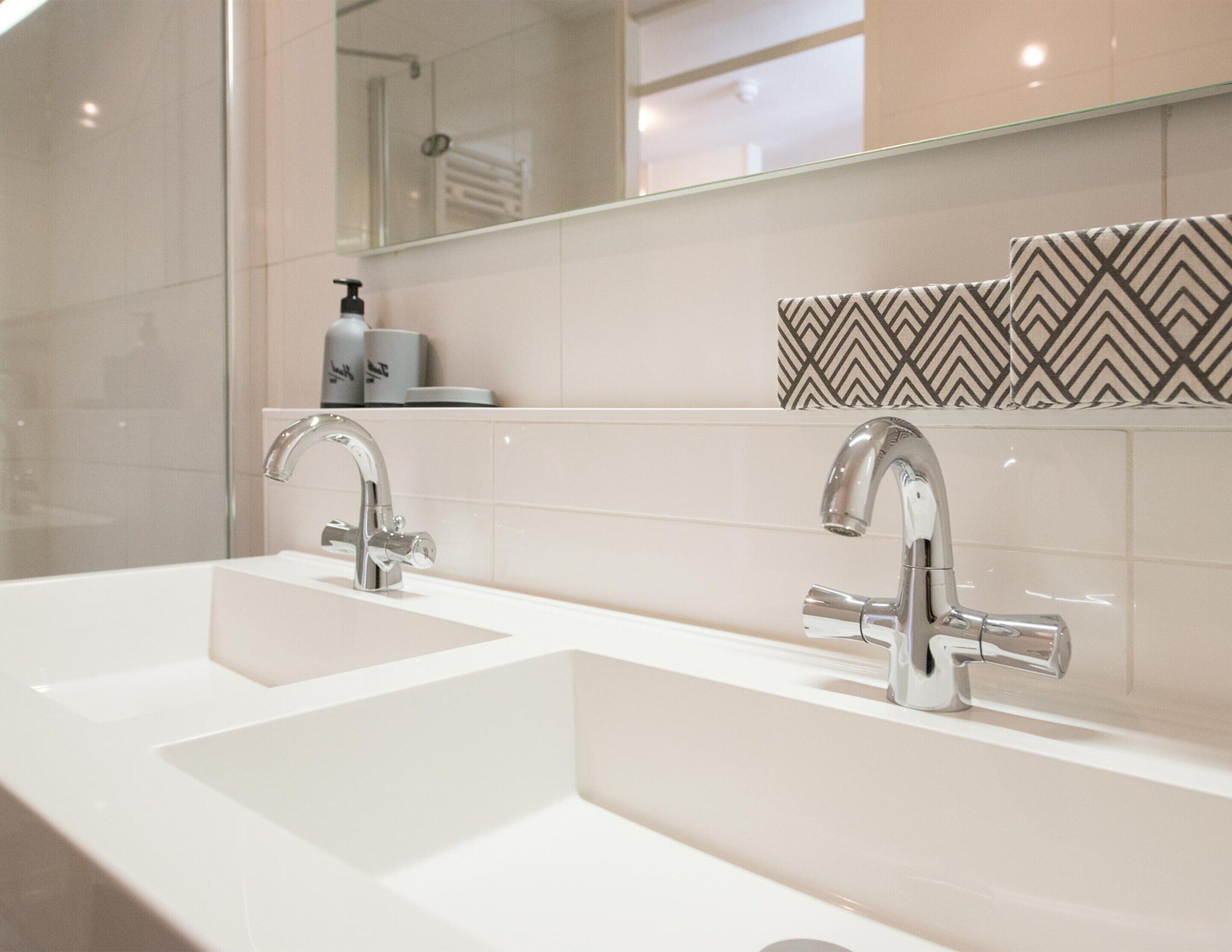 A modern bathroom with two sinks, a large mirror, and a patterned tile backsplash.