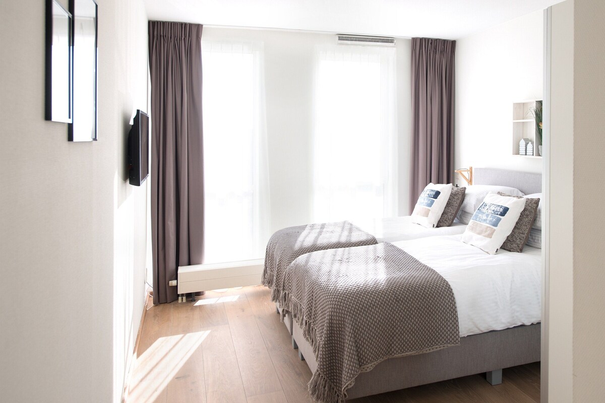 A modern bedroom with a bed, a TV, and a window with curtains.