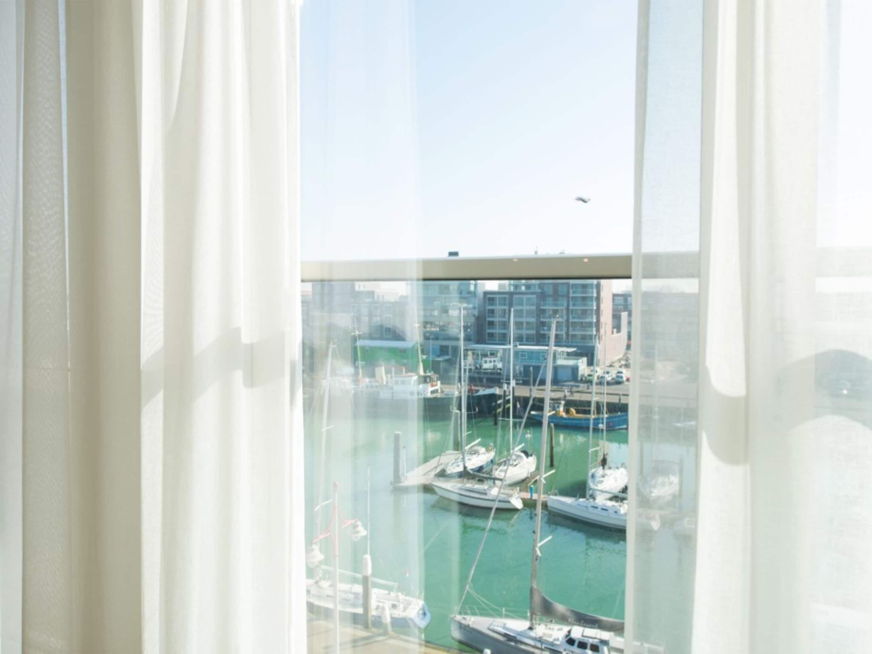 Vista de um porto com barcos atracados, céu claro e edifícios ao fundo.