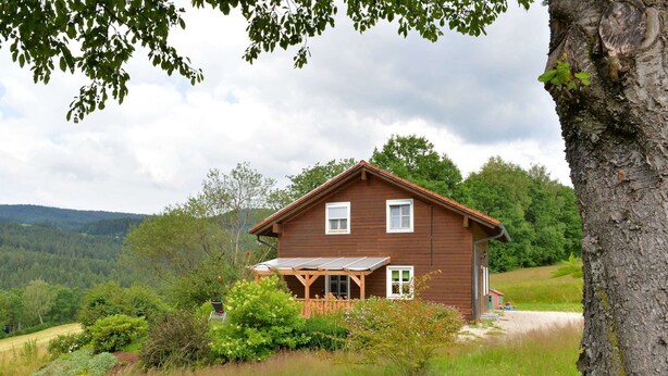 Een houten huis met een veranda, omringd door groen en heuvels.