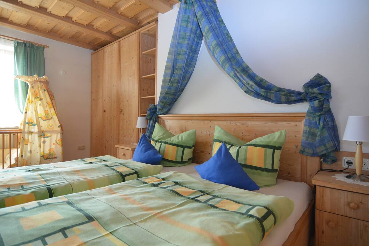 A room with two beds, wooden headboards, and a large window with curtains.