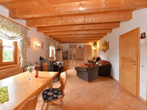 A cozy living room with wooden beams, a dining area with a table and chairs, and a TV in the background. - Comfort Apartment With Balcony in the Beautiful Bavarian Forest (Drachselsried)