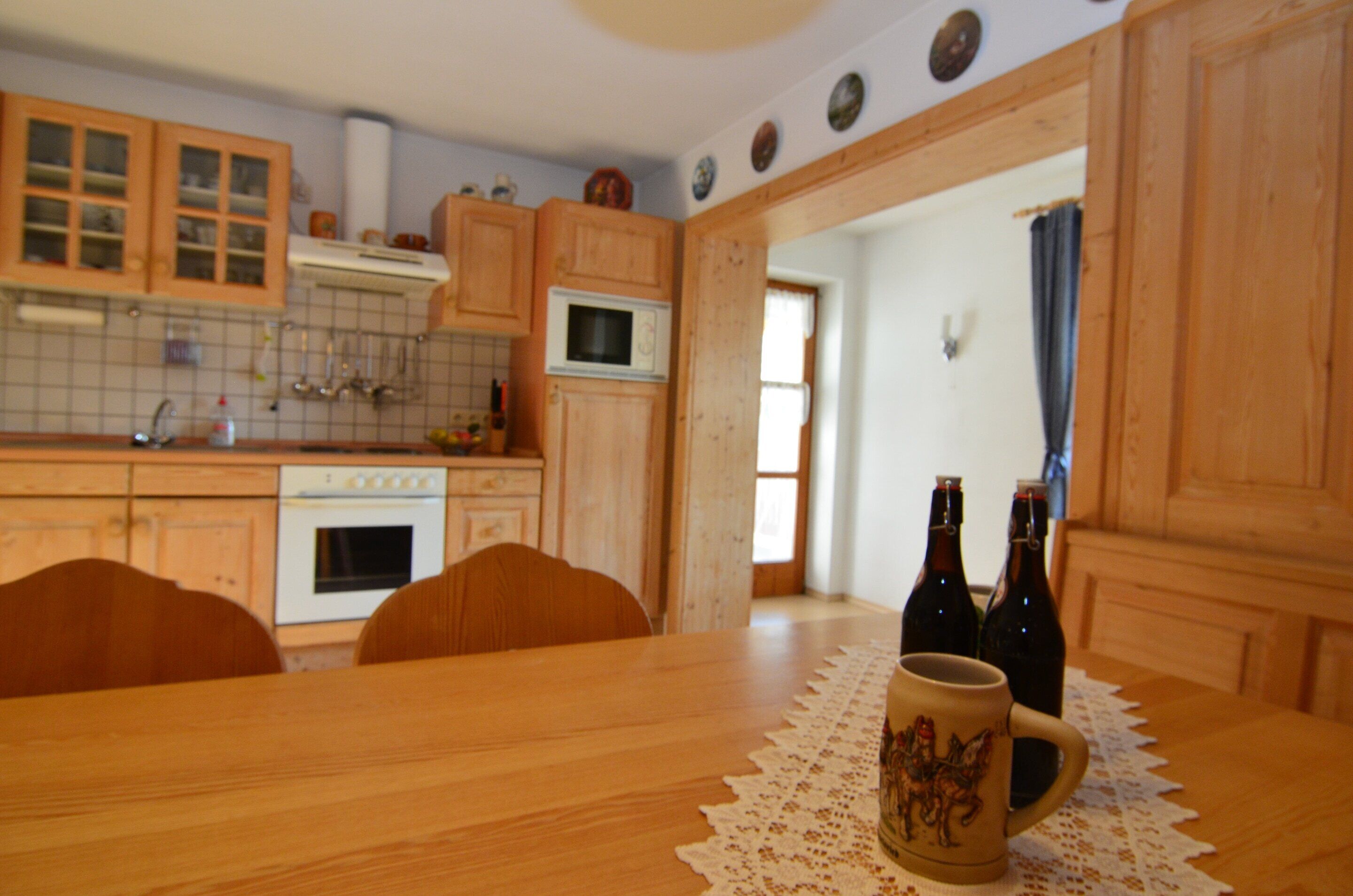 A kitchen with wooden cabinets, a stove, and a dining table with a lace tablecloth. There are two bottles on the table.