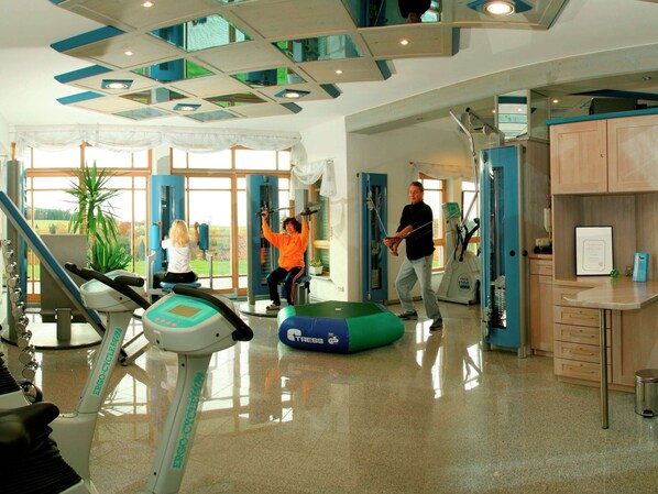 Un gimnasio con máquinas de cardio, una pelota de ejercicio verde y una persona usando una máquina de poleas.