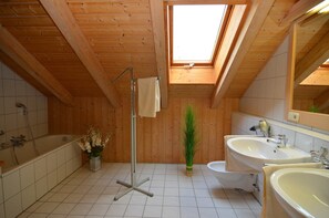 Un bagno con rivestimento in legno, un lucernario, una vasca da bagno, due lavandini e un water.