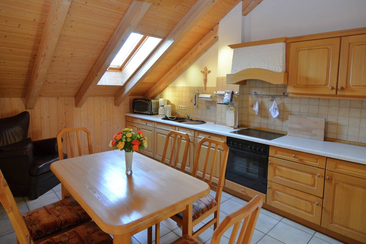 A cozy kitchen with wooden cabinets, a dining table with chairs, and a visible oven.