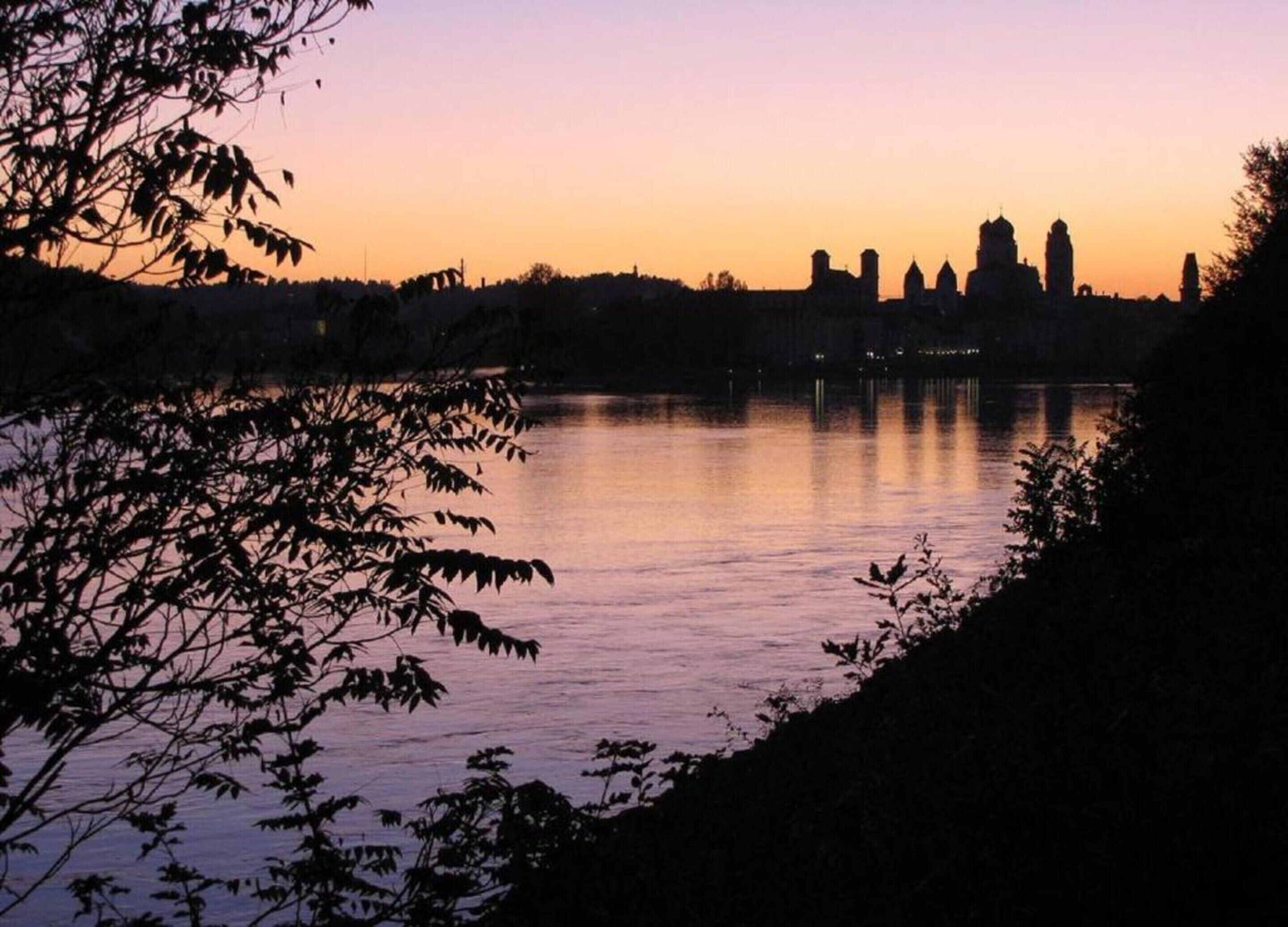 A serene lakeside view with a silhouette of a historic building complex against a sunset sky.