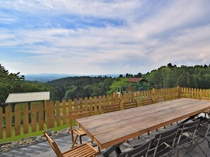 Tavolo e sedie di legno all'aperto, con vista su una zona boschiva e un piccolo edificio sullo sfondo.