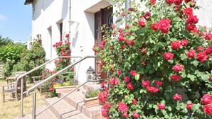 A white building with a staircase leading to a door, surrounded by red roses and a garden. - Inviting Apartment in Wendelstorf With Communal Garden (Bastorf)