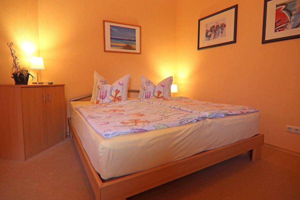 A bedroom with a wooden bed, two bedside lamps, a nightstand with a lamp, and a wall-mounted power outlet.
