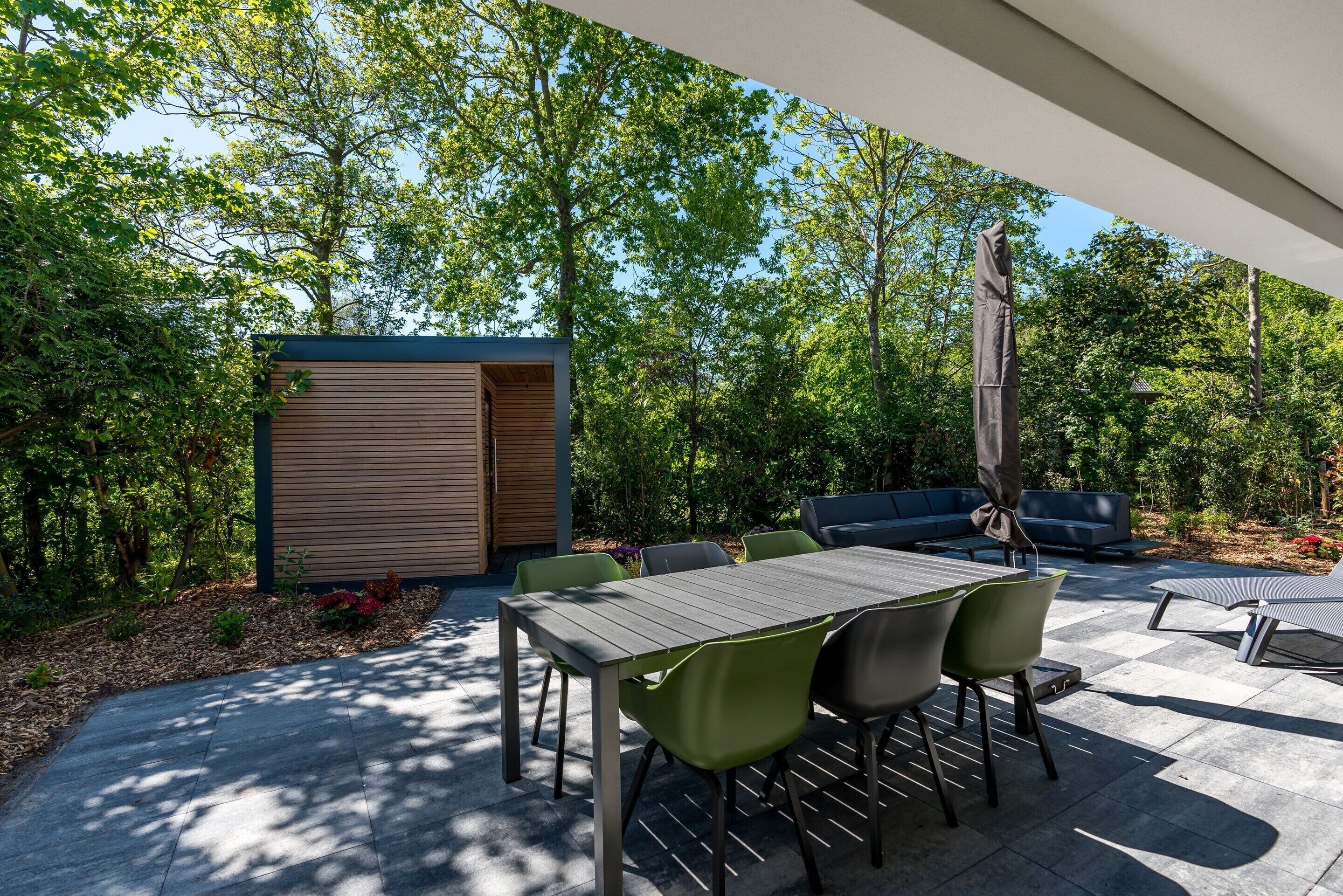 Un patio al aire libre con una mesa y sillas, rodeado de follaje y una estructura de madera.