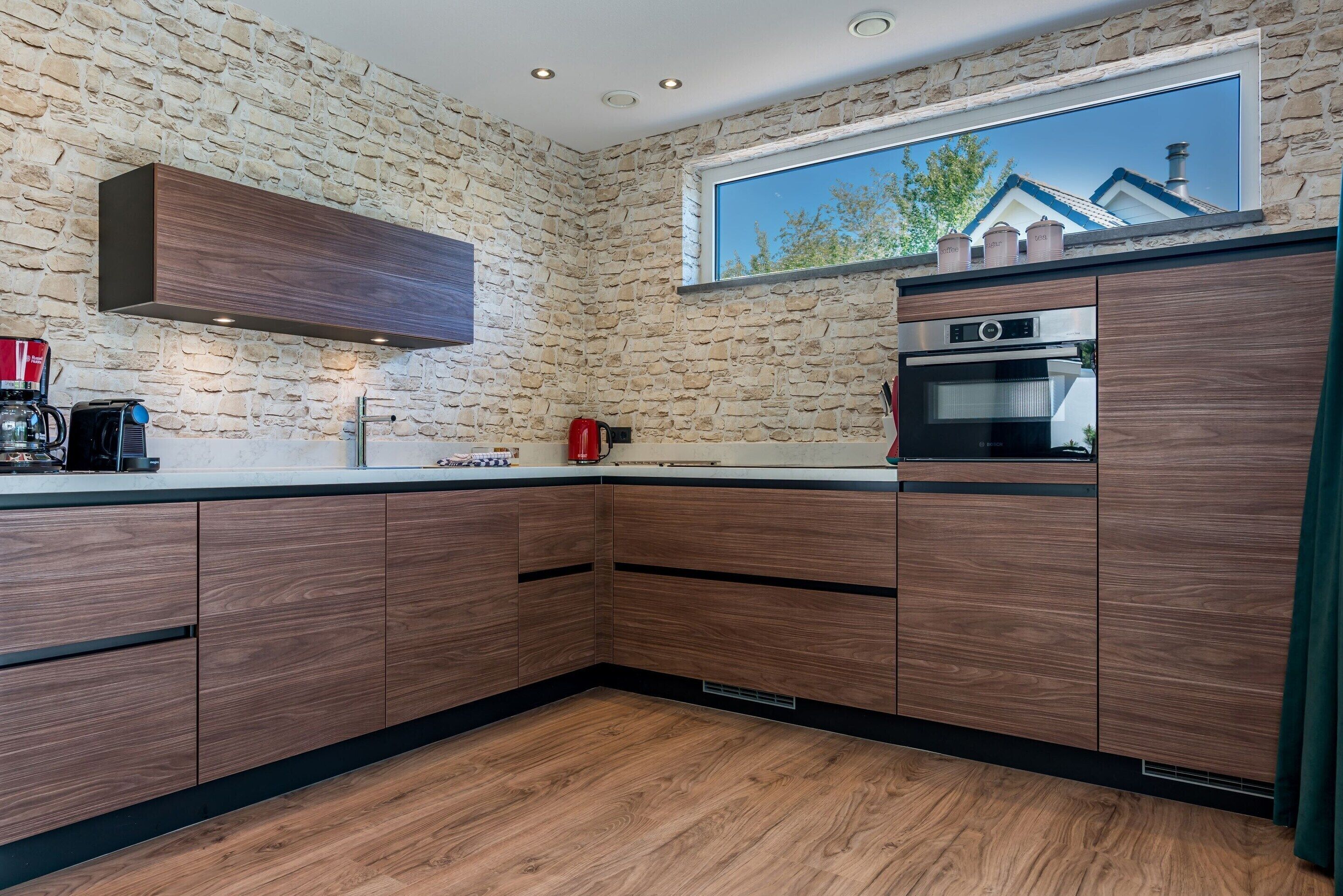 Una cocina con armarios de madera, horno empotrado y ventana con vistas a una casa.