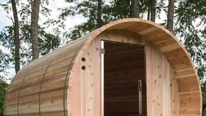 Eine zylindrische Holzhütte mit Tür, kleinem Fenster und einer Sitzbank im Inneren.