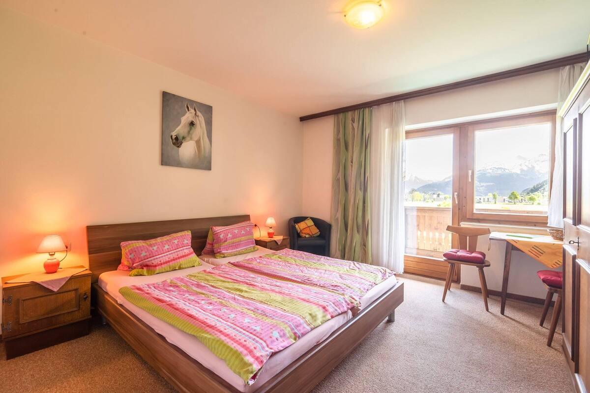 Een slaapkamer met een groot bed, een bureau, een stoel en uitzicht op bergen door het raam.