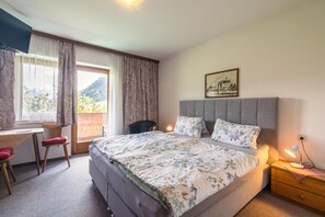 Une chambre à coucher comprenant un lit, un bureau, une chaise, une table de chevet et une fenêtre avec des rideaux.