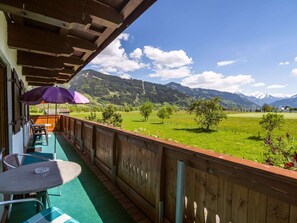 Un balcon en bois avec une table et des chaises, donnant sur un champ verdoyant et des montagnes.