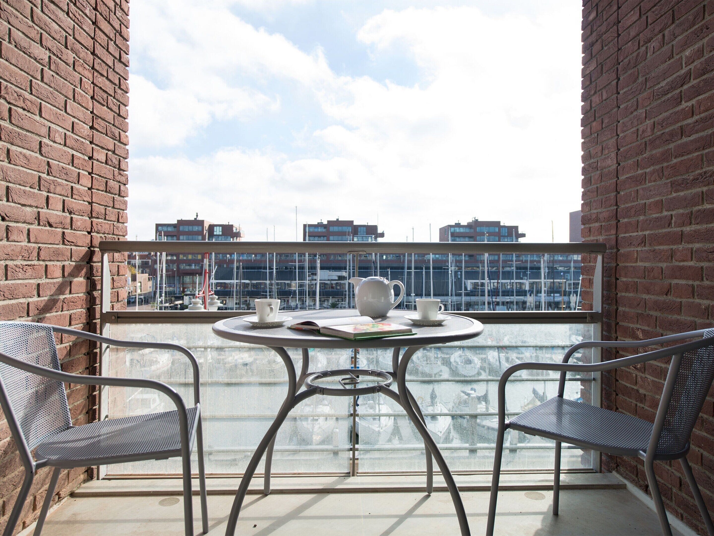 A balcony with two metal chairs, a small round table, and a white teapot.