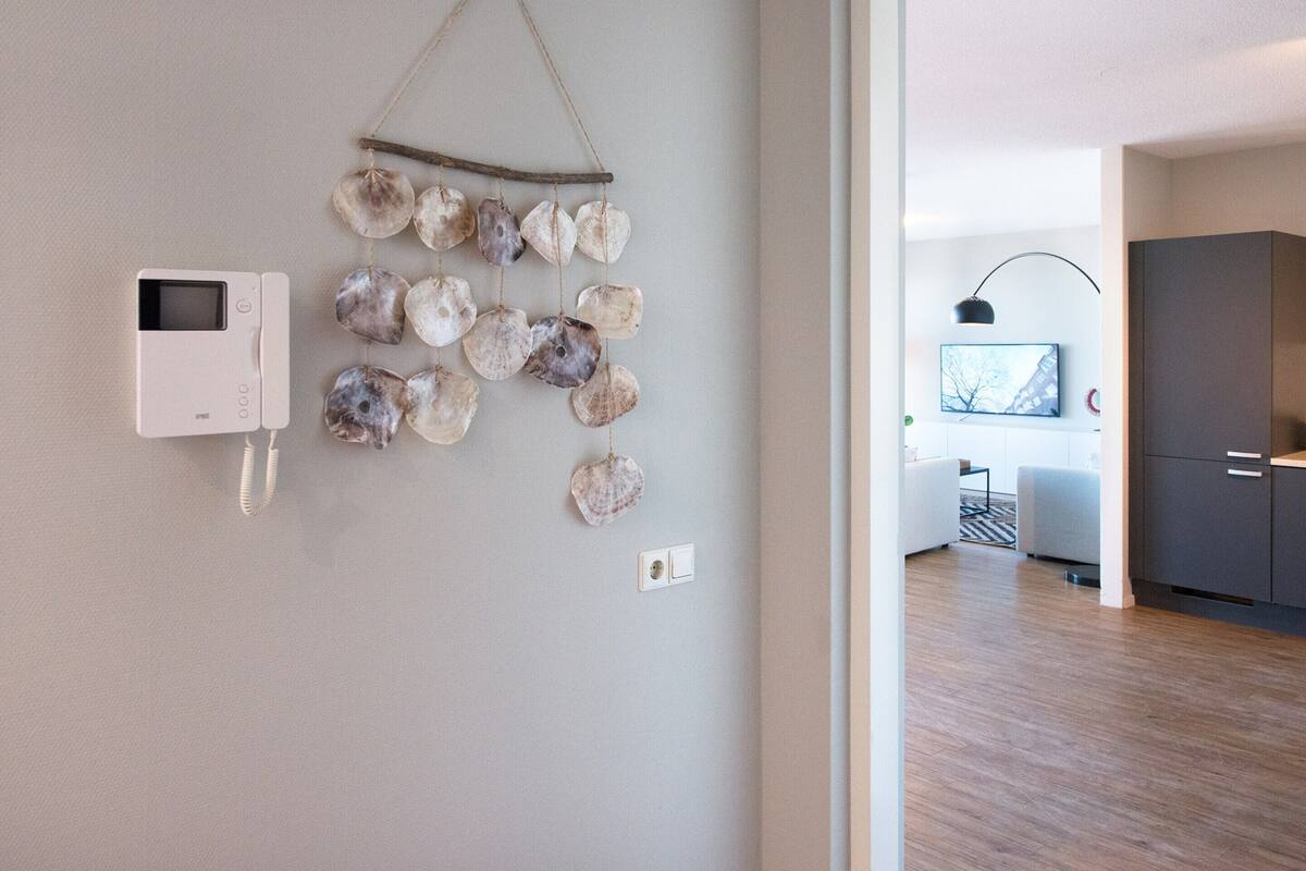A modern interior with a wall-mounted decorative shell arrangement, a white intercom, and a glimpse of a living area with a TV and furniture.