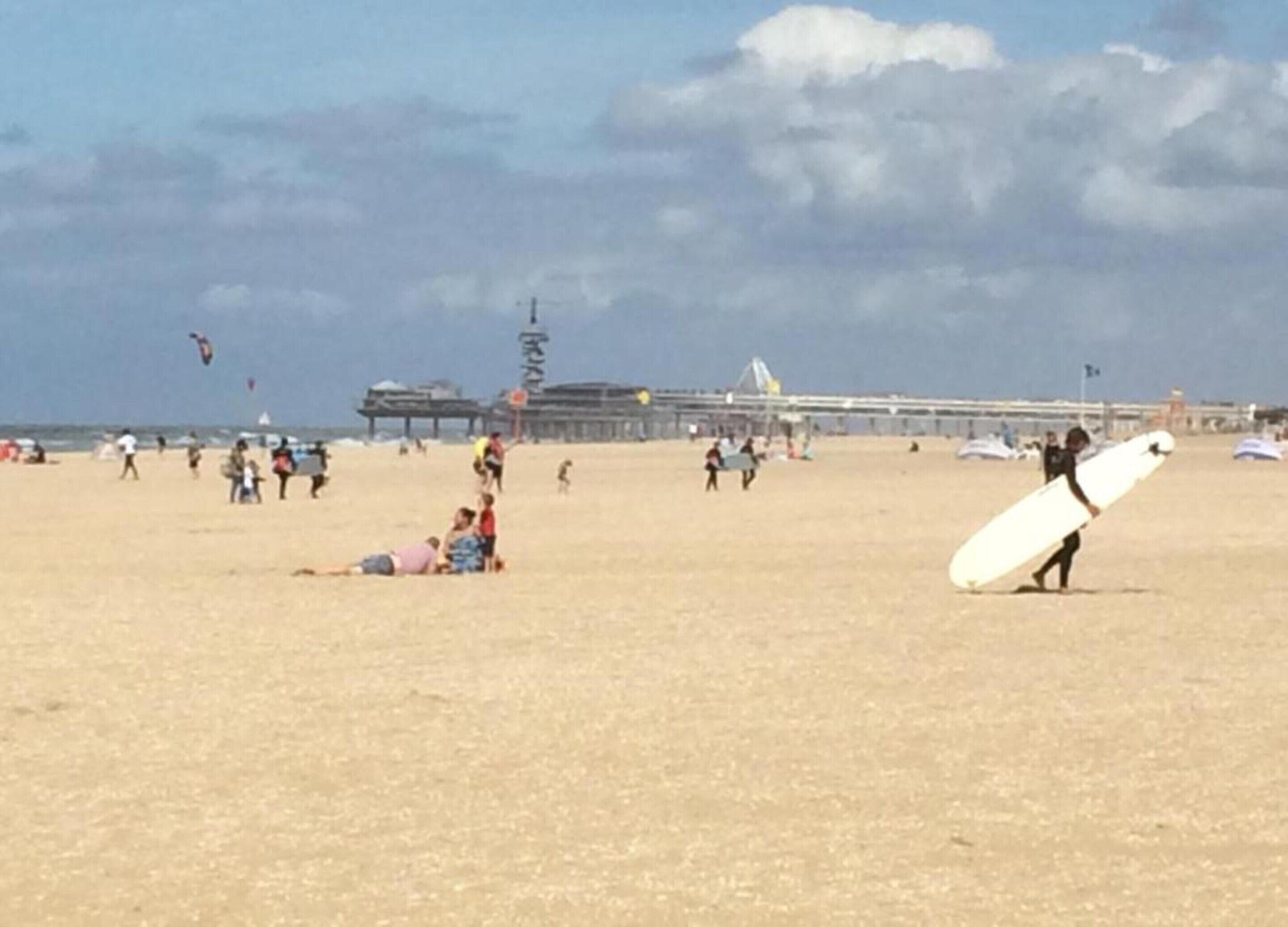 A beach with people, a pier, and a lifeguard tower.