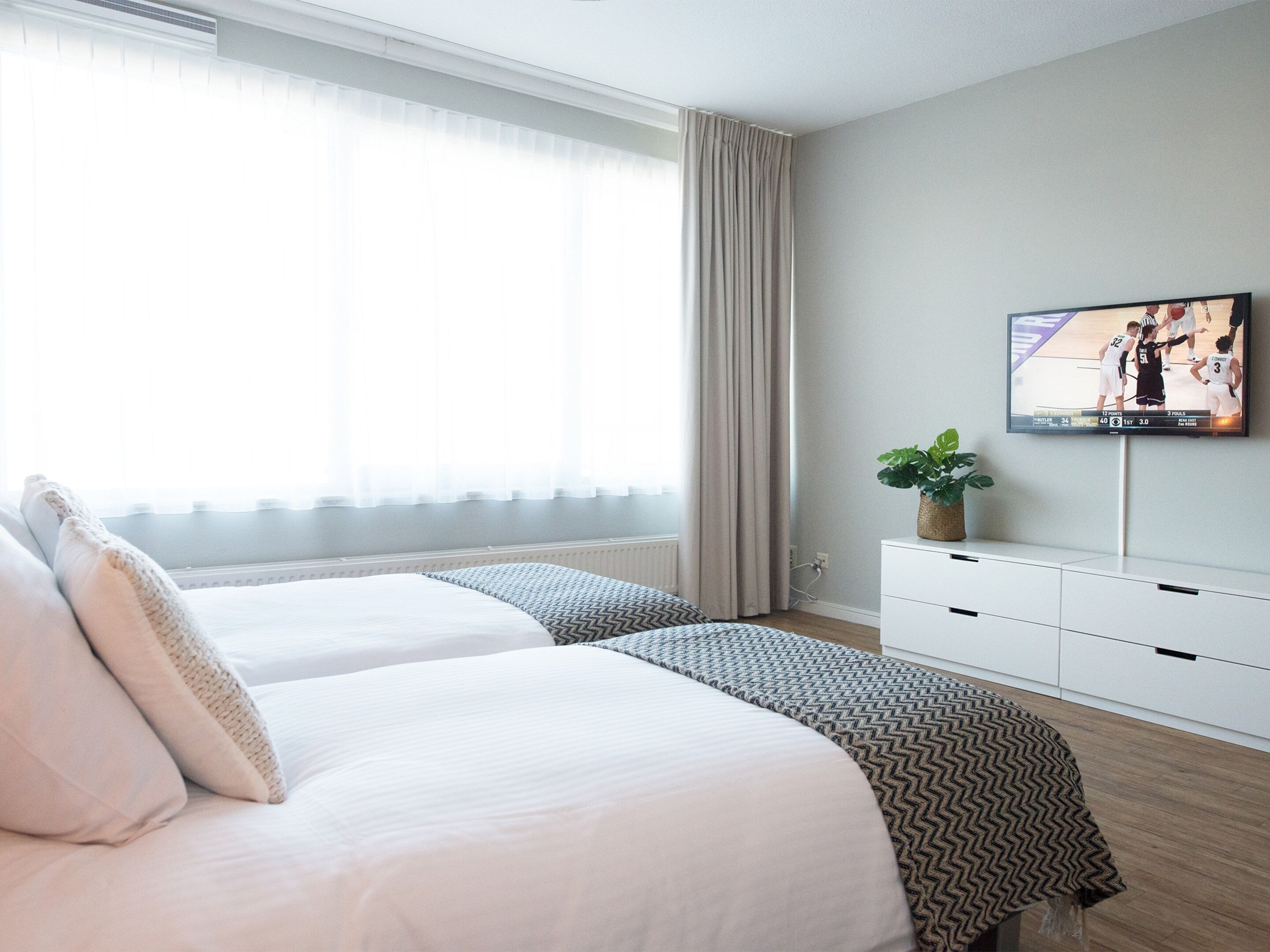 Una camera d'albergo con due letti, una TV a parete e una finestra con tende.