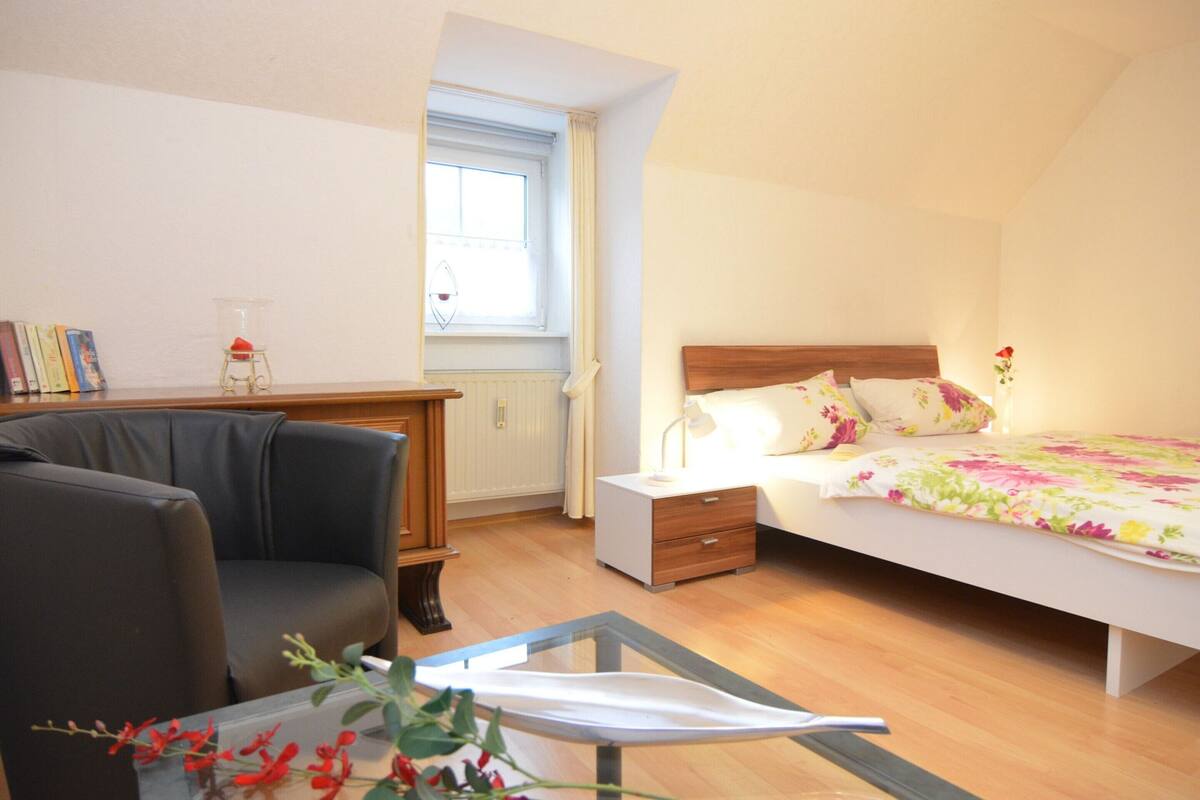 A bedroom with a bed, bedside table, lamp, and a chair.
