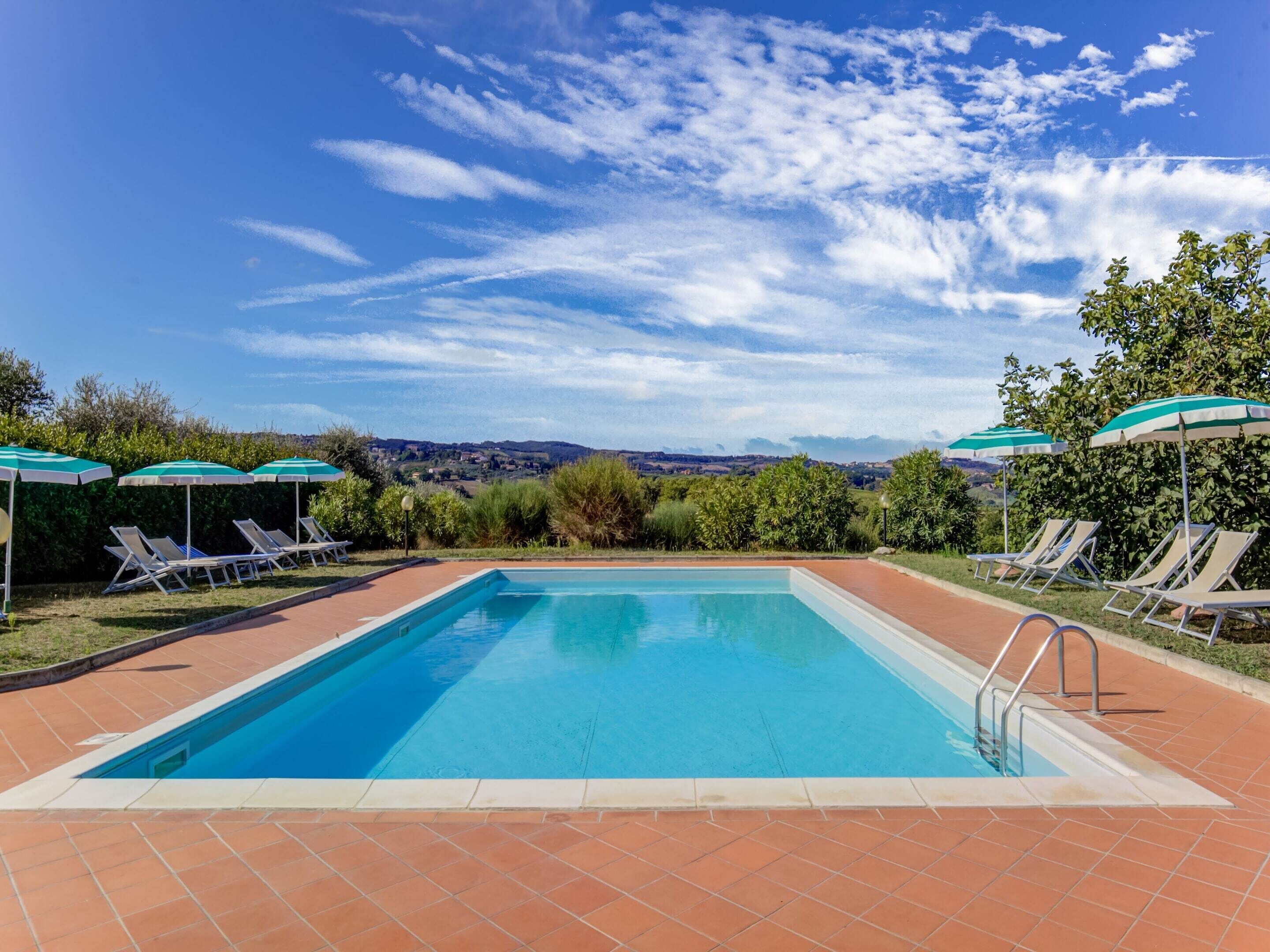 A rectangular swimming pool with a tiled border, surrounded by lounge chairs and umbrellas.