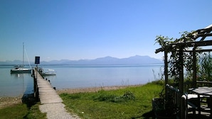Vista del lago con un muelle de madera que lleva a los botes, una zona de picnic y montañas al fondo.