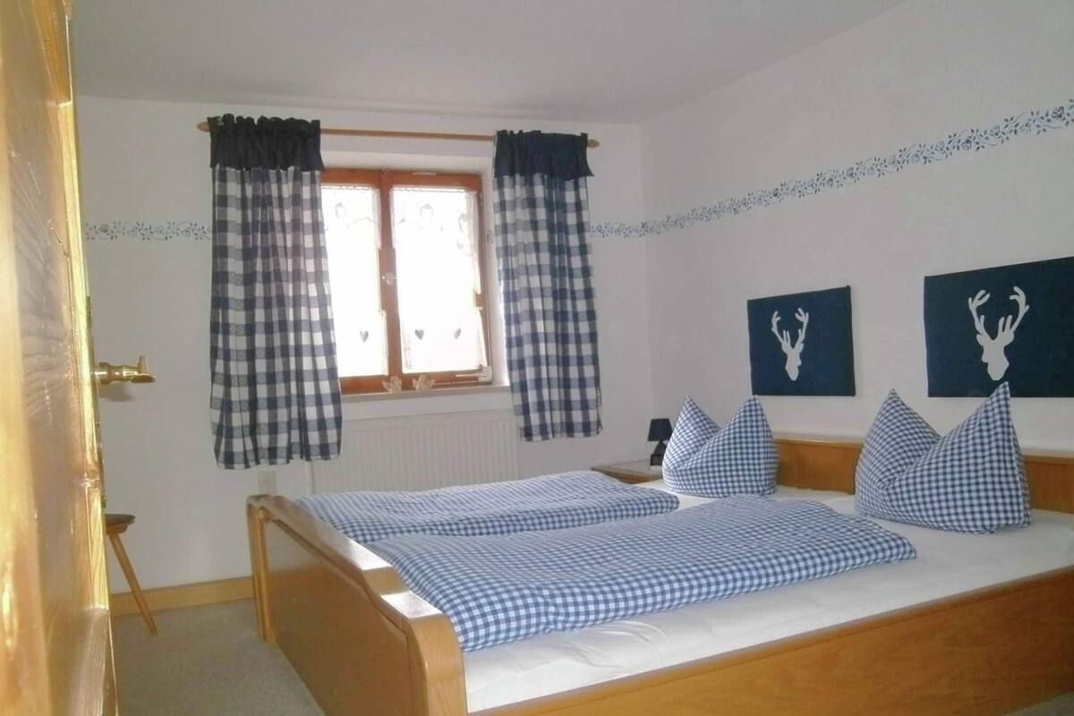 A bedroom with a wooden bed, checkered curtains, and two wall-mounted deer head decorations.