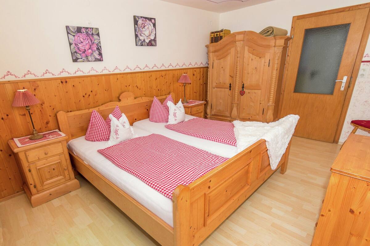 A wooden bed with checkered bedding, a nightstand with a lamp, a wardrobe, and two floral wall decorations.