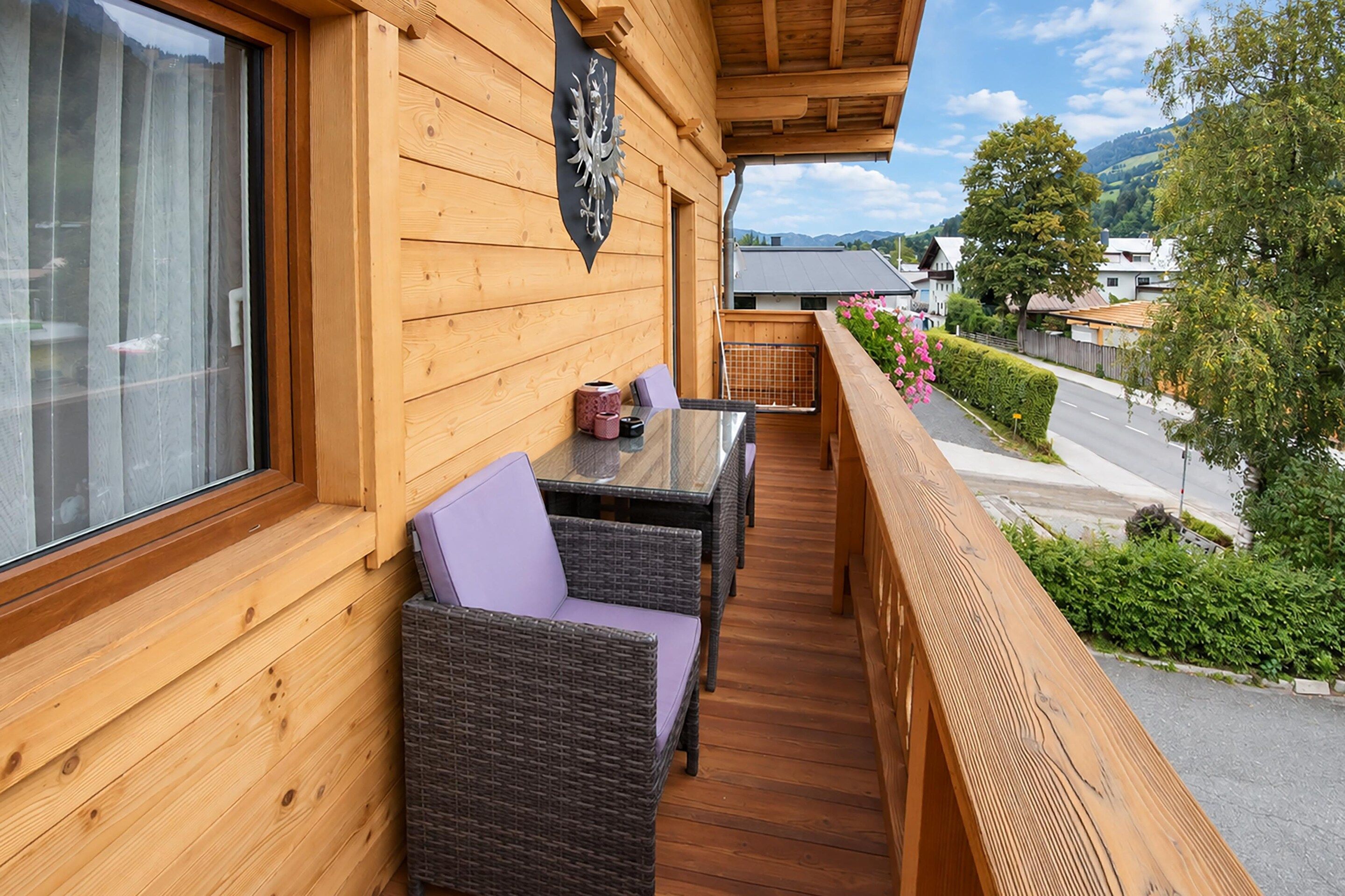 A wooden balcony with wicker furniture, a decorative metal emblem, and a view of a residential street.