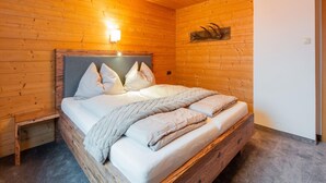 A wooden-paneled bedroom with a bed, bedside table, and wall-mounted light fixture. - Modern Apartment in Kitzbuhel Near Ski Area (Kitzbuhel)